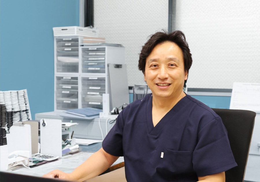 診察室の机に向かい微笑む院長